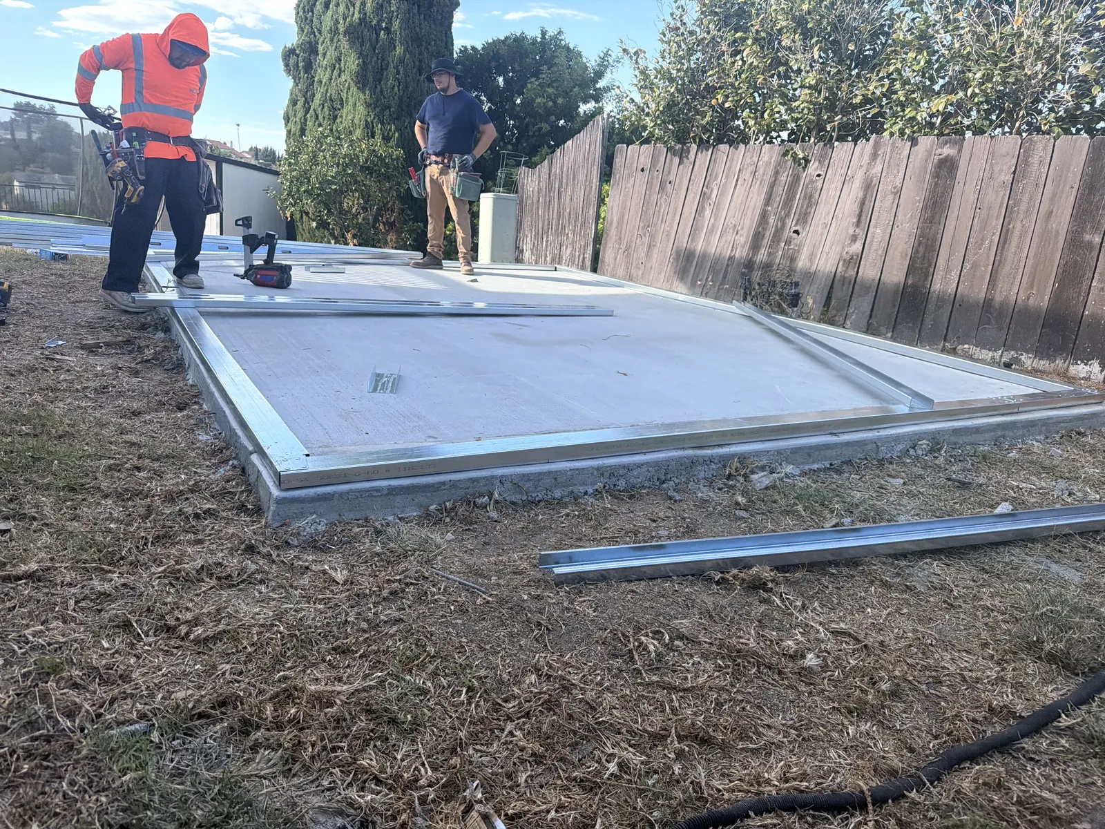 Construction crew laying out galvanized steel framing on a concrete slab